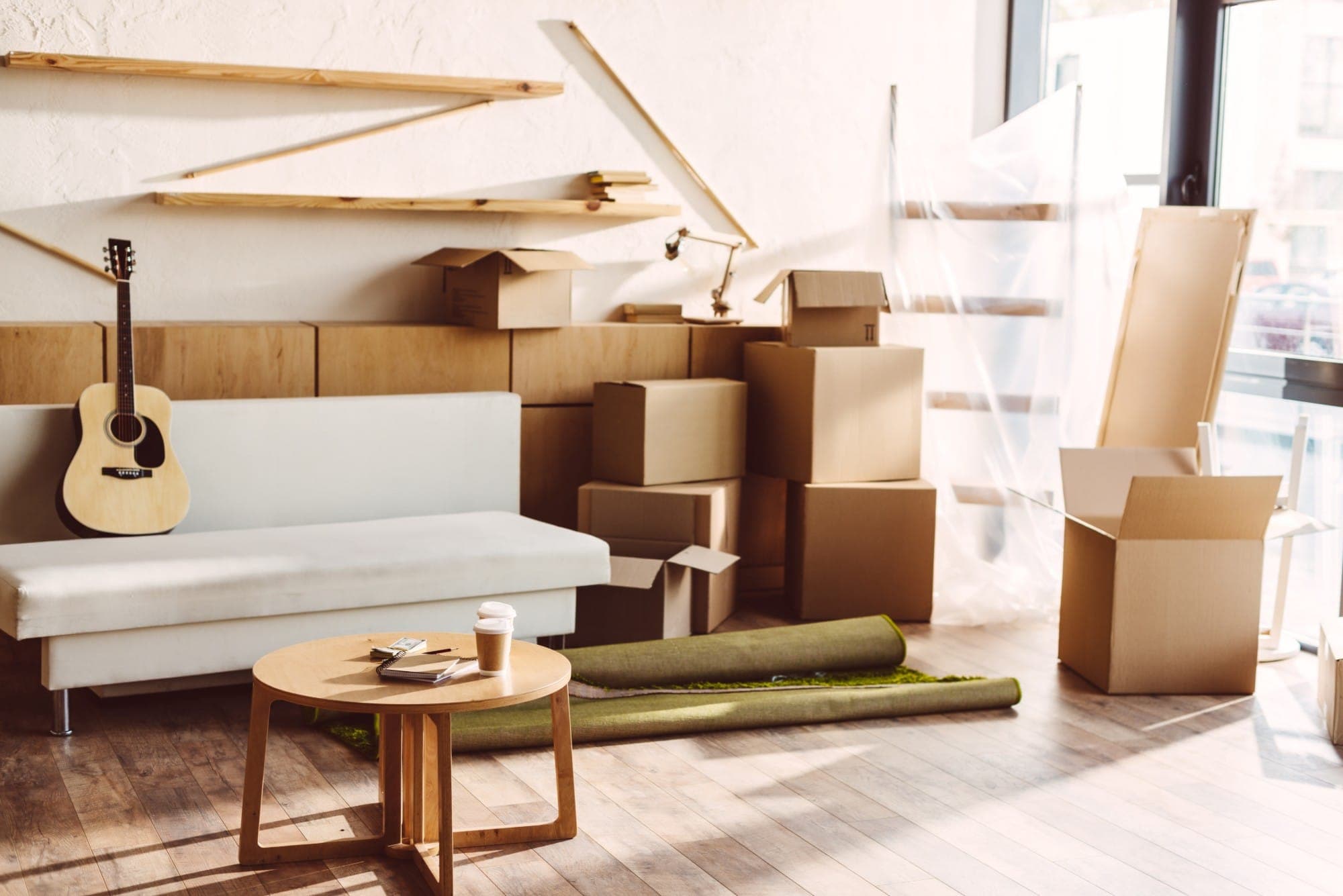 Wohnzimmer mit Sofa, Umzugskartons und aufgerolltem Teppich – bereit für den Umzug